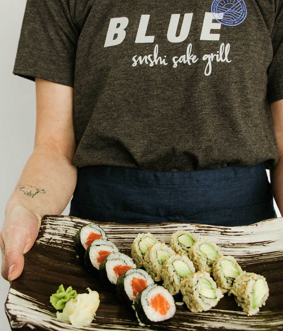 Female in Blue Sushi Sake Grill tee with sushi platter.